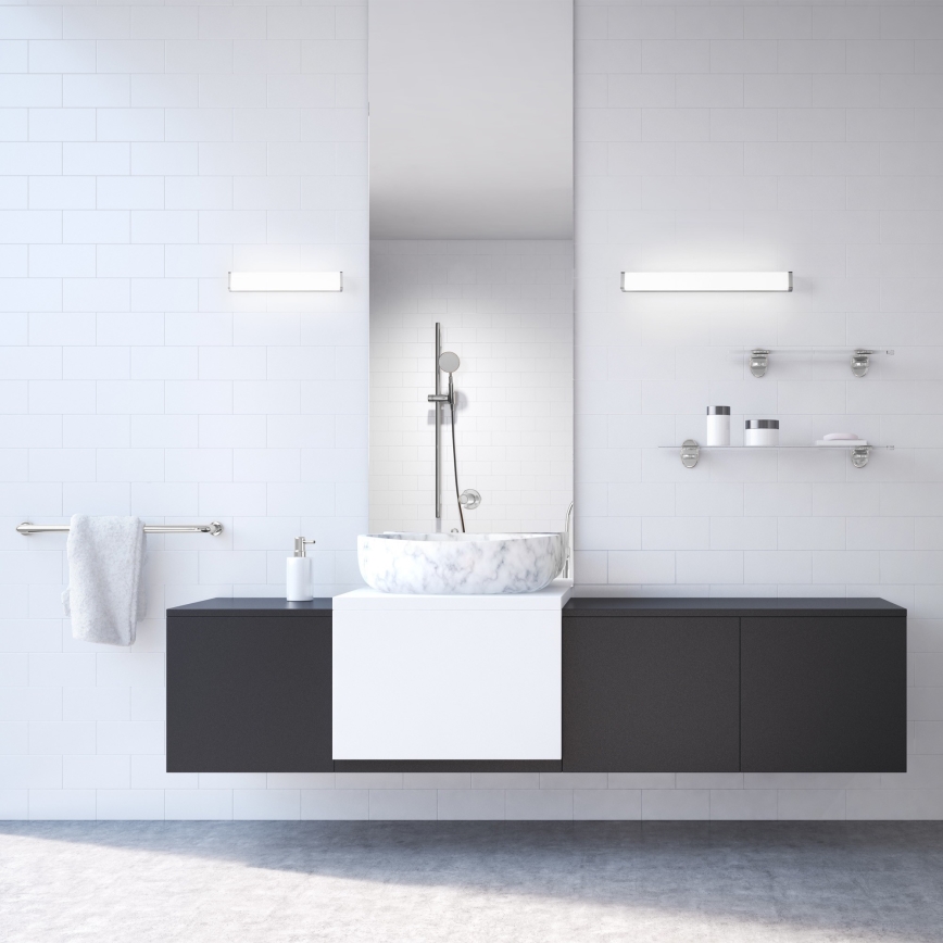 Mramorové umývadlo je umiestnené na tmavošedej skrinke v kúpeľni. Kúpeľňa má biele obklady a dve sklenené police s kozmetikou.