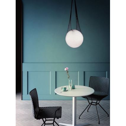Guľová lampa visí zo stropu na čiernych šnúrkach. Je umiestnená nad bielym okrúhlym stolom s dvoma čiernymi stoličkami v jedálni s tyrkysovými stenami.
