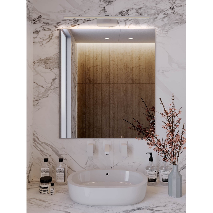 Zrkadlo osvetlené LED pásom umiestnené nad umývadlom v kúpeľni s mramorovým obkladom. Vedľa umývadla sú kozmetické výrobky a váza s vetvičkami.