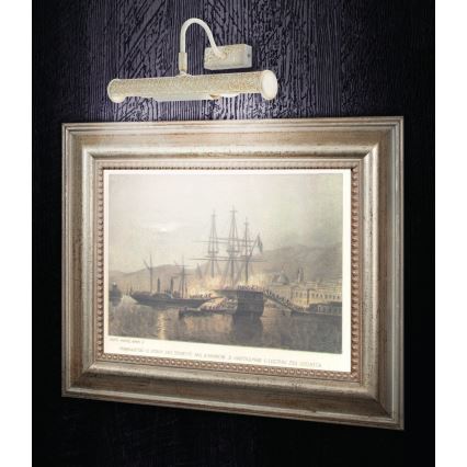 Svietidlo osvetľuje obraz v ráme. Obraz zobrazuje námornú scénu s loďami v prístave. Svietidlo je pripevnené na stene. Text pod obrázkom je nečitateľný.