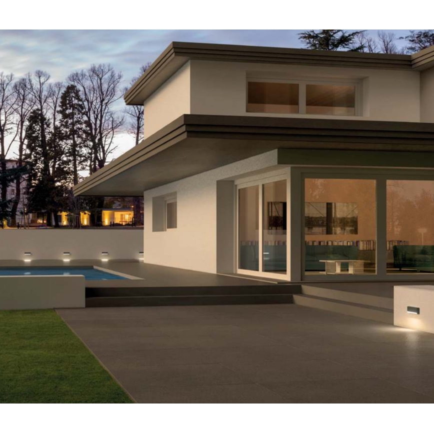 Moderná vila s bazénom je osvetlená zabudovanými svetlami. Svetlá sú umiestnené pri bazéne a na vonkajšej stene budovy. Na fotografii je vidieť vonkajšie priestory vily v súmraku.