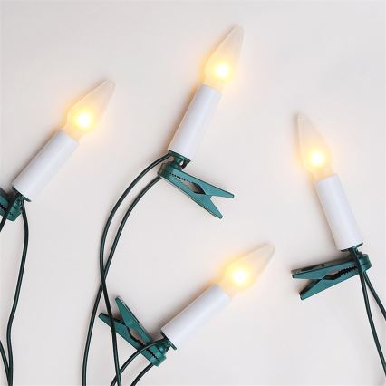 Štyri LED sviečky pripevnené zelenými sponkami na kábel. Sviečky sú biele s teplým žltým svetlom. Svetlá sú umiestnené na svetlom pozadí.
