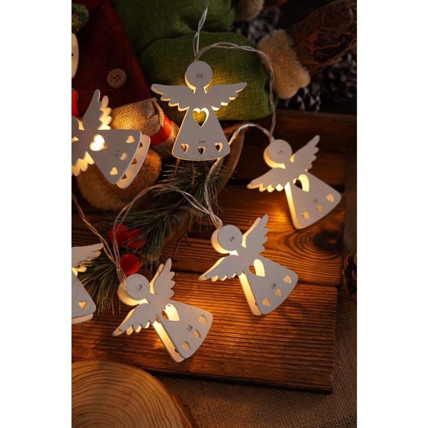 Svetielkujúce drevené anjlíky tvarované ako siluety s vyrezávanými srdiečkami sú zavesené na svetelnom reťazi. Svetlá svietia v tmavšom prostredí na drevenom povrchu.