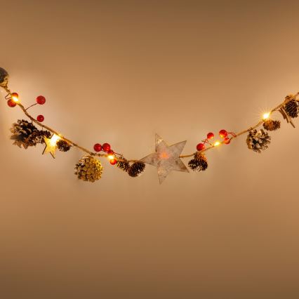 Svetlá s dekoráciami visia v oblúku. Súčasťou dekorácie sú šišky, hviezdičky a červené bobule. Svetlá sú zapnuté, na hnedom pozadí.