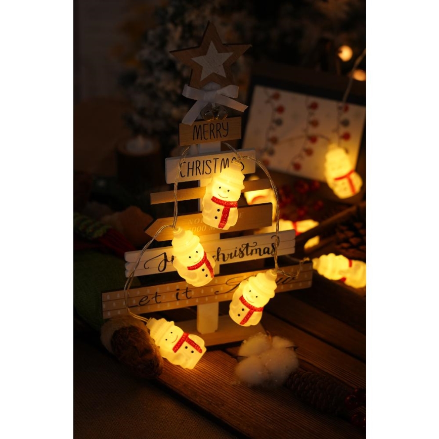 Svietiace snehuliakové svetielka s motívom snehuliaka sú omotané okolo dreveného vianočného stromčeka. Na stromčeku je napísané: „Merry Christmas“ a „Joy Christmas“.