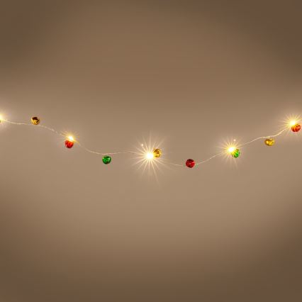 Svetielkový veniec s malými farebnými ozdobami vo forme zvončekov v červenej, zelenej a zlatej farbe visí pred hnedým pozadím. Žiarovky svietia.