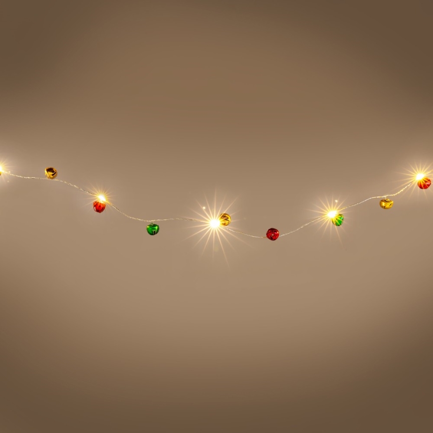 Svetielkový veniec s malými farebnými ozdobami vo forme zvončekov v červenej, zelenej a zlatej farbe visí pred hnedým pozadím. Žiarovky svietia.