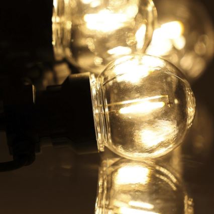 Guľatá LED žiarovka svieti. Je pripojená k čiernemu držiaku a nachádza sa na odrazovej ploche. V pozadí sú ďalšie rozžiarené žiarovky.