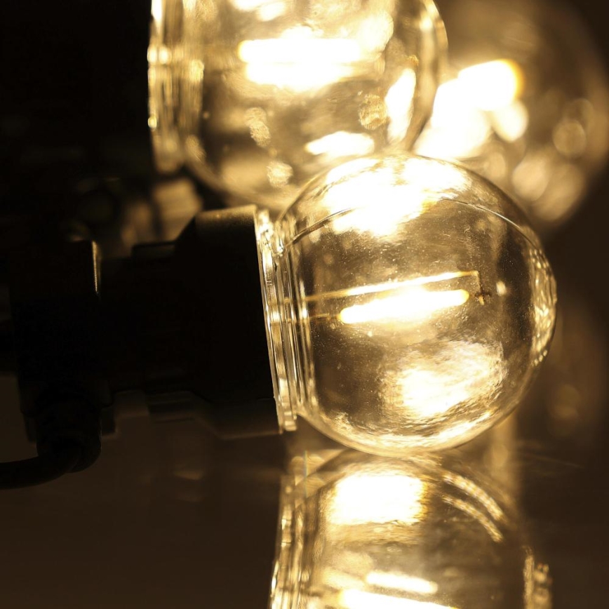 Guľatá LED žiarovka svieti. Je pripojená k čiernemu držiaku a nachádza sa na odrazovej ploche. V pozadí sú ďalšie rozžiarené žiarovky.