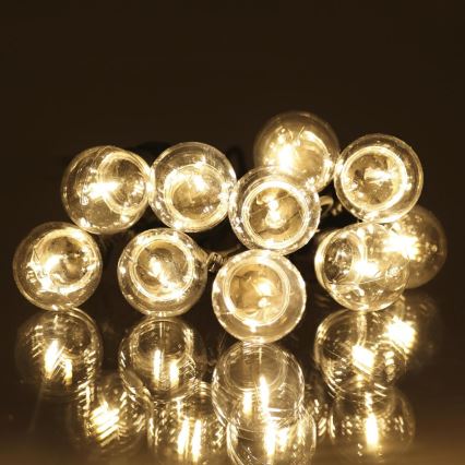Guľové LED žiarovky svietia. Sú spojené do svetelného reťazca. Ležia na odrazivej tmavej ploche.