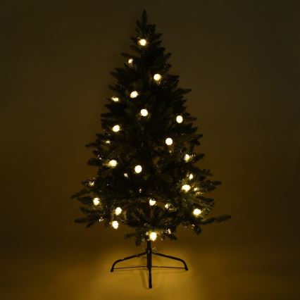 Vianočný stromček svieti. Svetlá s teplou bielou farbou sú rozmiestnené po konároch. Stromček stojí na čiernom stojane v tmavej miestnosti.
