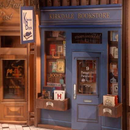 Miniatúrny model kníhkupectva „Kirkdale Bookstore“ s výkladmi plnými kníh. Na dverách je adresa „9 Passage des Panoramas“ a otváracia doba. Pred kníhkupectvom sú malé drevené boxy s knihami.