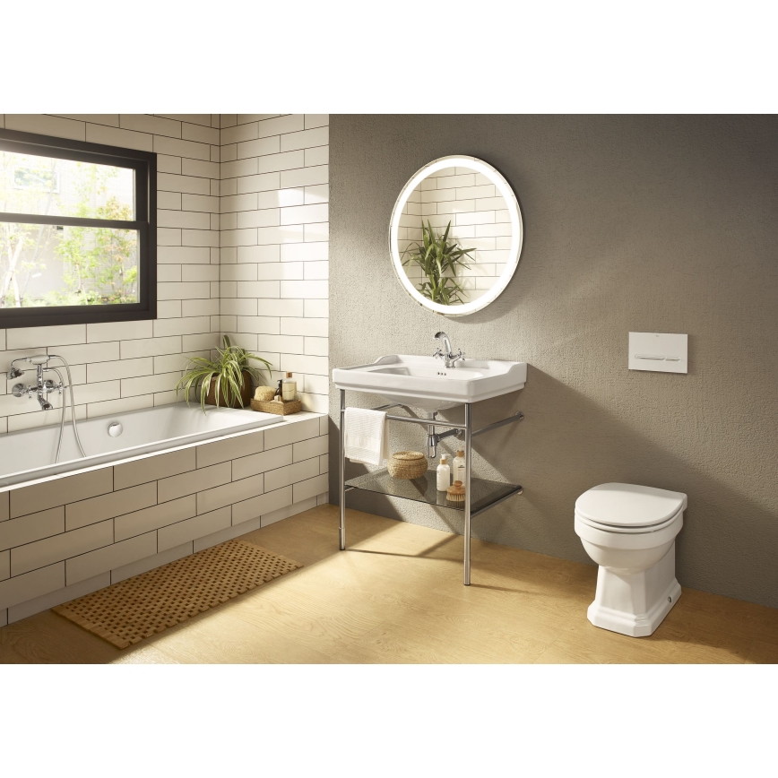 Umyvadlo stojí na kovovom stojane s poličkou v kúpeľni. V kúpeľni je vaňa, záchod a okrúhle zrkadlo s LED osvetlením. Steny sú obložené bielymi obkladačkami. Podlaha je drevená.