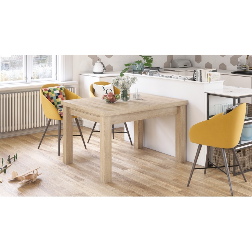 Obdĺžnikový jedálenský stôl zo svetlého dreva stojí v kuchyni. Pri stole sú dve žlté stoličky. Kuchyňa má bielu linku a drevenú podlahu.