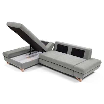 Rohová sedačka s otvoreným úložným priestorom v sivej látke s drevenými nožičkami. Sedačka je rozkladacia. Je umiestnená na bielom pozadí.