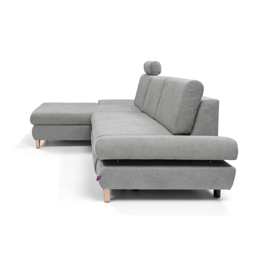 Rohová sedačka s opierkou hlavy je umiestnená na bielom pozadí. Sedačka je sivá, má drevené nožičky a obsahuje samostatný podnož.