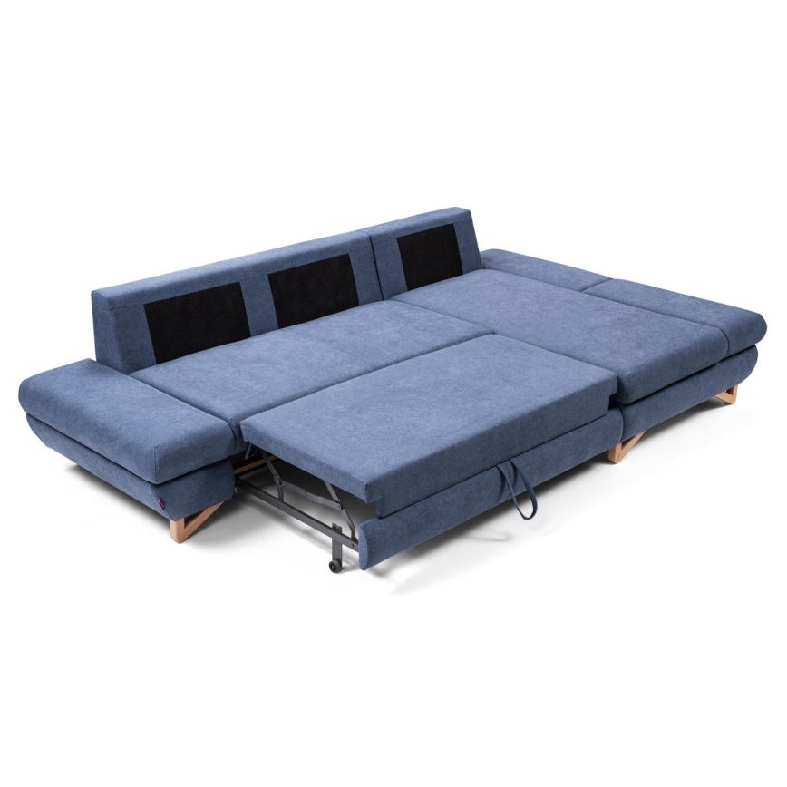 Rohová sedačka s rozkladacím mechanizmom sa rozkladá. Je tmavomodrej farby, má drevené nožičky a čierne detaily na operadlách. Sedačka je na bielom pozadí.