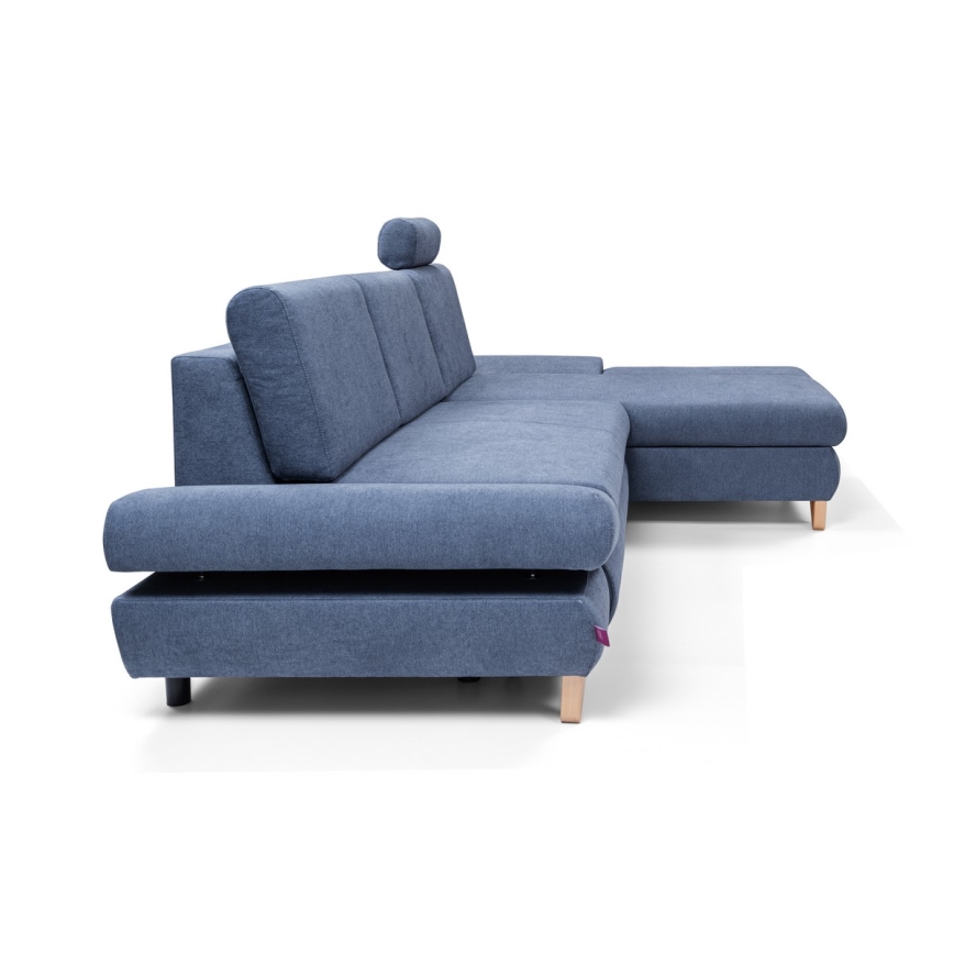 Rohová sedačka svetlomodrej farby stojí na svetlom drevenom podstavci. Sedačka má opierky a dodatočný opierkový vankúš. Je umiestnená na bielom pozadí.