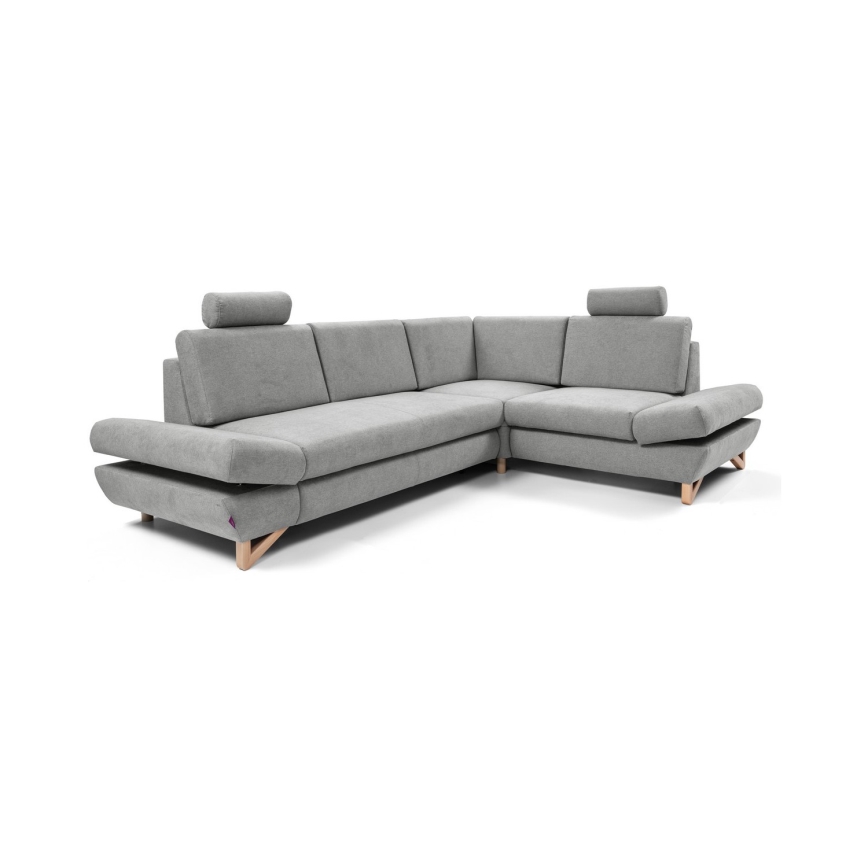 Rohová sedačka stojí v obývacej izbe. Sedačka je sivá, má drevené nohy a opierky hlavy. Nachádza sa na svetlej podlahe, pred ňou je konferenčný stolík a koberec. Za sedačkou je stena s dekoráciou zo špaličiek dreva.