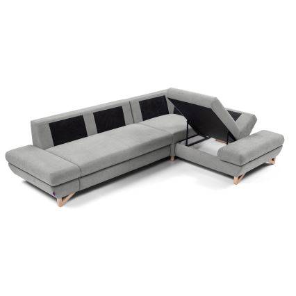 Rohová sedačka s odkladacím priestorom má otvorenú úložnú časť. Sedačka je sivá s tmavými vankúšikmi. Je umiestnená na bielom pozadí.