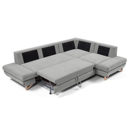 Rohová sedačka s rozkladacím mechanizmom sa rozkladá. Sedačka je sivá s čiernymi detailmi, má drevené nožičky a je umiestnená na bielom pozadí.