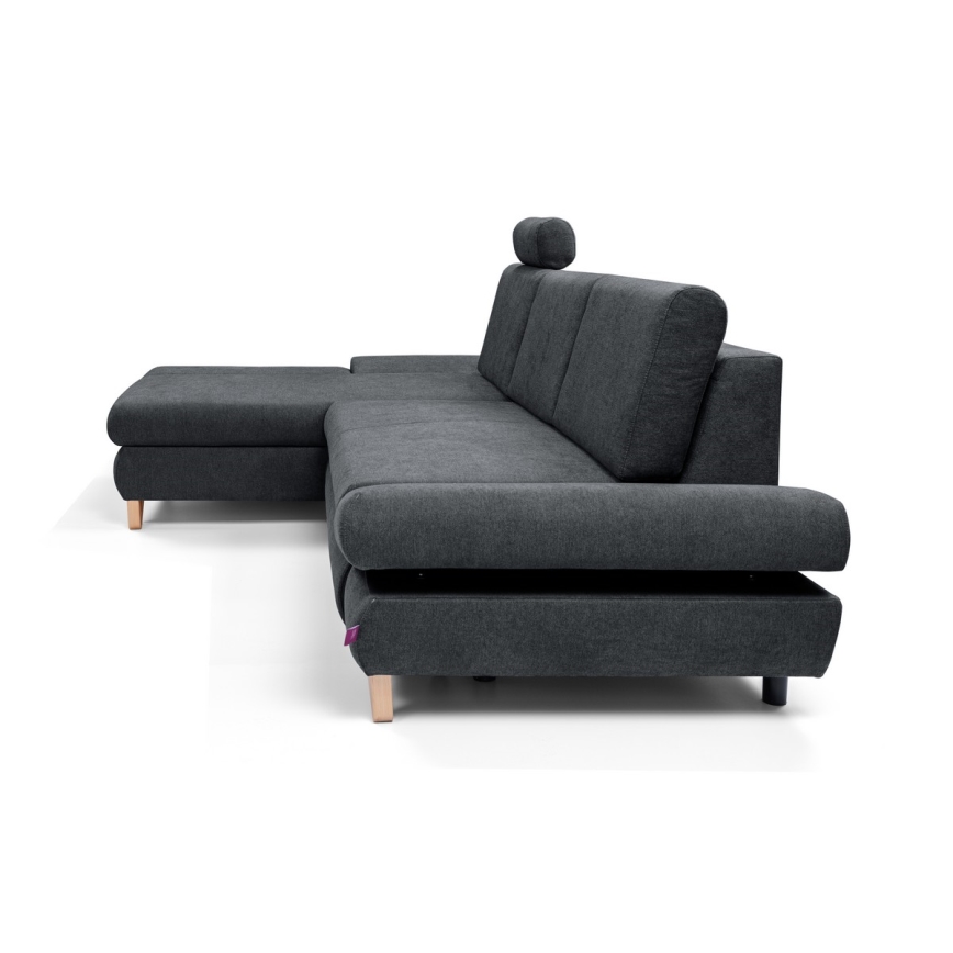 Rohová sedačka s opierkou hlavy stojí na bielom pozadí. Sedačka je tmavosivá, látková, s drevenými nožičkami a obsahuje aj samostatný taburet.