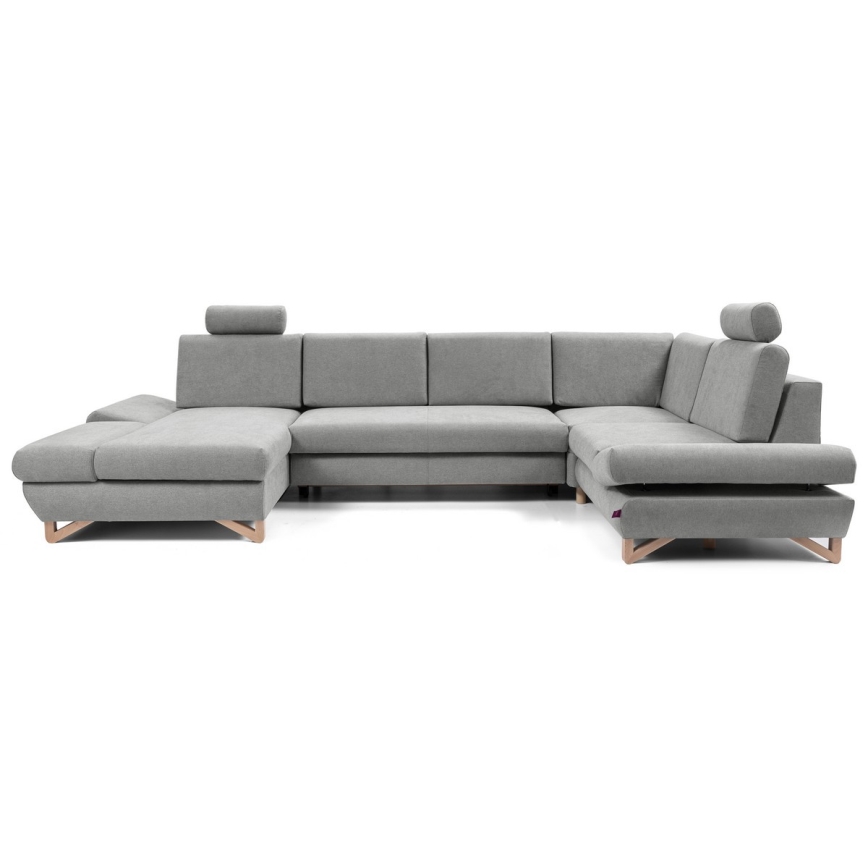 Rohová sedačka stojí na bielom pozadí. Sedačka je sivá, má drevené nohy a opierky hlavy. Je rozsiahla a tvarom pripomína písmeno U.