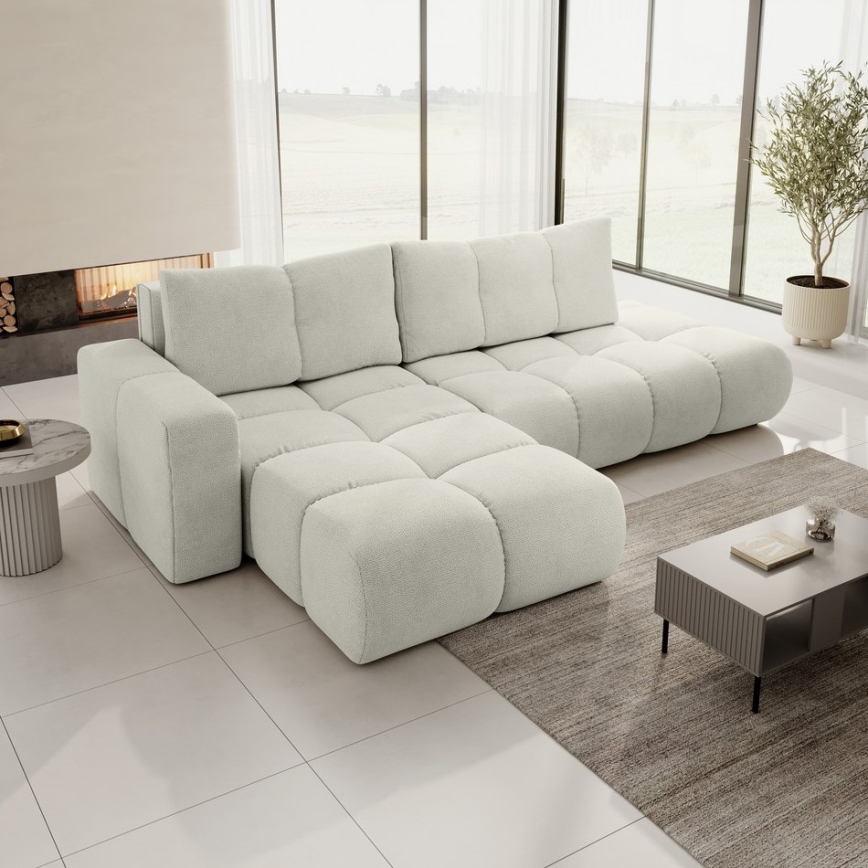 Rohová sedačka je umiestnená na bielom pozadí. Sedačka je svetlo béžová, s výrazným prešívaním. Má rozsiahly sedací priestor s opierkami a nápaditým tvarom.