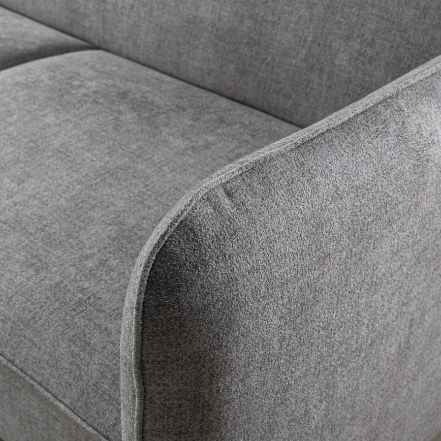 Sivá pohovka s jemnou textúrou poťahu, zaoblenými lakťovými opierkami, je detailne zobrazená. Zobrazený je detail opierky a časti sedadla.