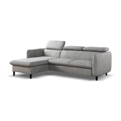 Rohová sedačka v sivej látke stojí v moderne zariadenej obývacej izbe. Sedačka má rohovú časť a opierky. Pred sedačkou je drevený konferenčný stolík. Izba obsahuje veľké okná a tmavé steny.