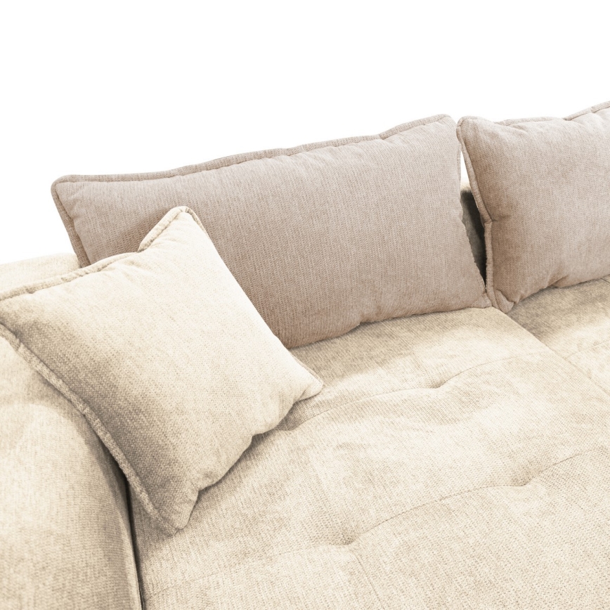 Rohová sedačka s vankúšmi odpočíva. Sedačka je svetlo béžovej farby, s niekoľkými väčšími a menšími vankúšmi v dvoch odtieňoch béžovej. Na obrázku nie je žiadny text.