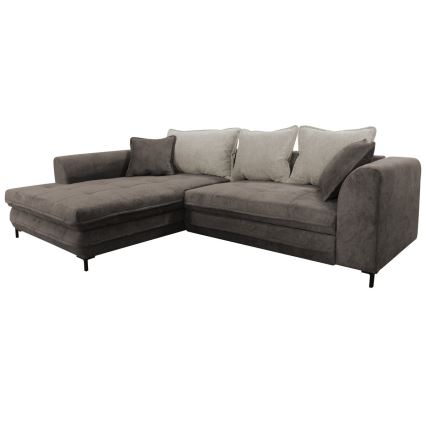 Rohová sedačka tmavošedej farby stojí v svetlej obývačke s drevenou komodou a kobercom. Sedačka má béžové vankúše a čierne nožičky. V popredí je konferenčný stolík s knihami a dekoráciami.