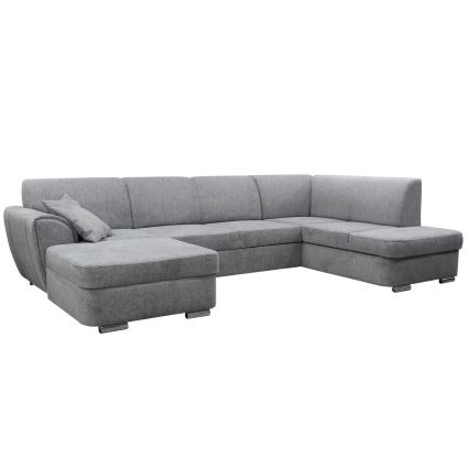 Rohová sedačka sivohnedej farby stojí v moderne zariadenej obývacej izbe s drevenou podlahou, kobercom a konferenčným stolíkom. Sedačka má ľavý roh a je doplnená o vankúš.