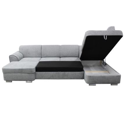Rohová sedačka s rozkladacím mechanizmom a úložným priestorom je odklopená. Sedačka je sivá, s tmavou výsuvnou časťou, na bielom pozadí.