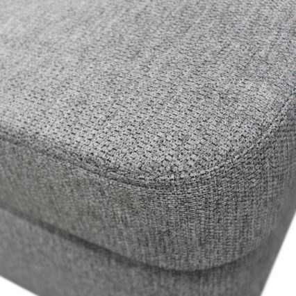 Sedacia časť nábytku – sivá textília s jemnou textúrou, vykazuje prešívanie po obvode. Je zhotovená z látky s výraznou štruktúrou.