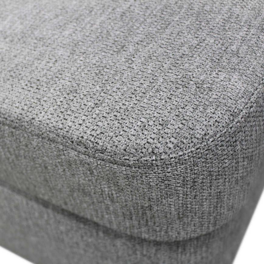 Sedacia časť nábytku – sivá textília s jemnou textúrou, vykazuje prešívanie po obvode. Je zhotovená z látky s výraznou štruktúrou.