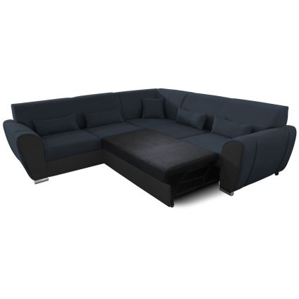 Rohová sedačka s rozkladacím lôžkom je v tmavomodrej látke s čiernymi detailmi. Lôžko je čiastočne vysunuté. Sedačka má niekoľko vankúšov a stojí na bielom pozadí.
