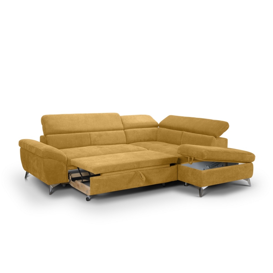 Rohová sedačka horčicovej farby s rozkladacím mechanizmom a úložným priestorom je umiestnená na bielom pozadí. Sedačka má pripojený menší taburet s úložným priestorom.