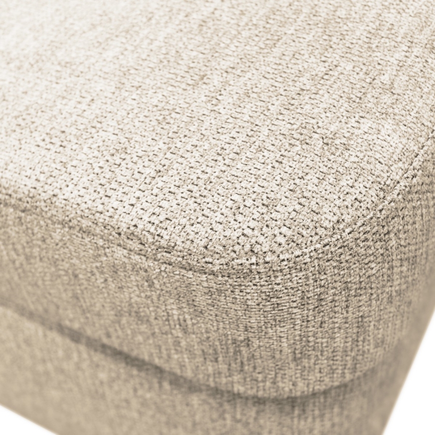 Čalúnená časť nábytku, pravdepodobne sedák, je vyrobená z béžovej textílie s jemnou textúrou. Je zhotovená z materiálu s viditeľným prepletením vlákien. Zobrazený je detail povrchu.