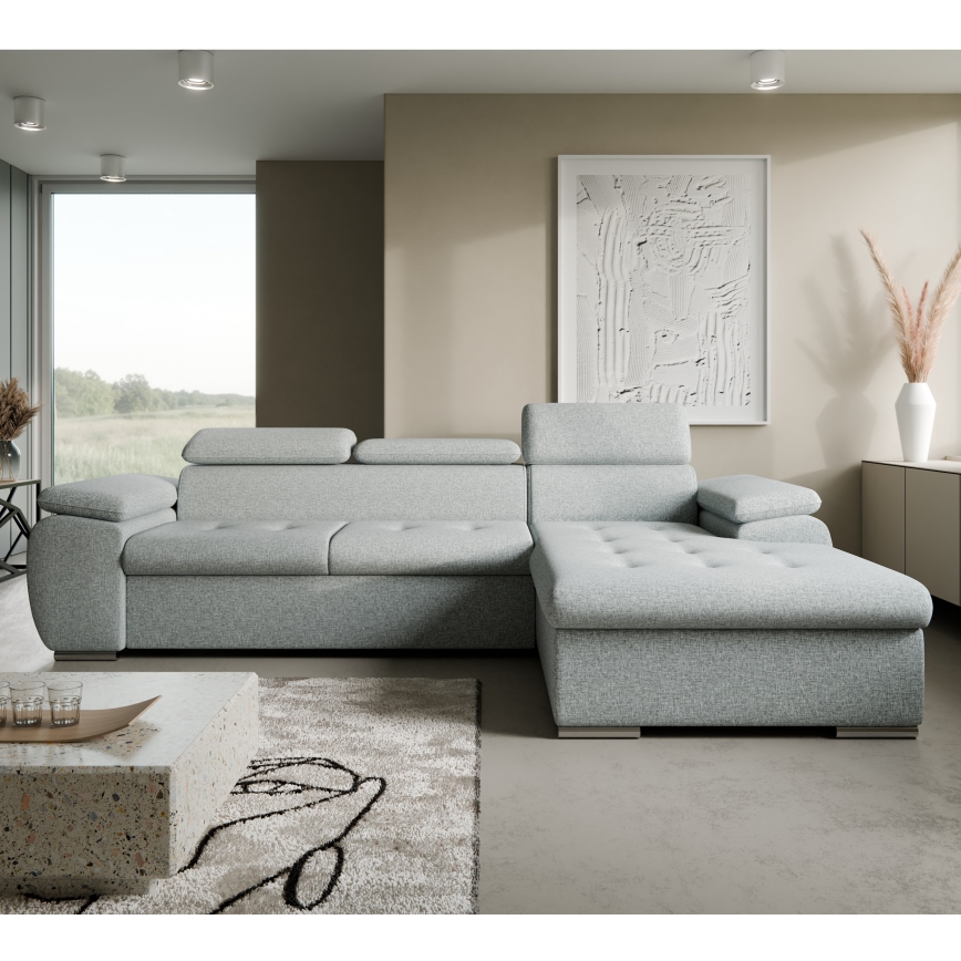 Rohová sedačka svetlosivej farby stojí na bielom pozadí. Sedačka má tri vankúše a je otočená doľava. Má moderný dizajn.
