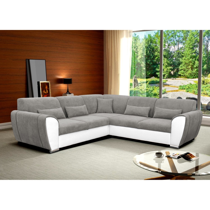 Rohová sedačka je umiestnená na bielom pozadí. Sedačka je čalúnená sivou a bielou látkou, má opierky na ruky a niekoľko vankúšov. Je to nábytok pre sedenie.