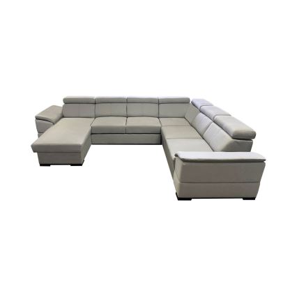 Rohová sedačka svetlošedej farby je umiestnená v priestrannej obývacej izbe s drevenou podlahou. Sedačka má niekoľko častí a je doplnená nízkym konferenčným stolíkom s drevenou doskou a kovovým rámom. V pozadí sú viditeľné okno, závesy a časť jedálenského stola.