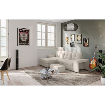 Rohová sedačka svetlo béžovej farby stojí v obývacej izbe. Sedačka má podnožku. V miestnosti je aj konferenčný stolík, koberec, gitara a reproduktory. Na stene visí plagát s portrétom Johna Lennona a text Give peace a chance.