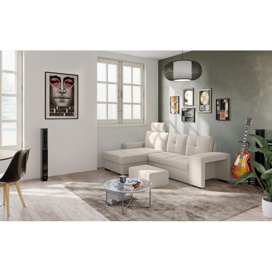 Rohová sedačka svetlo béžovej farby stojí v obývacej izbe. Sedačka má podnožku. V miestnosti je aj konferenčný stolík, koberec, gitara a reproduktory. Na stene visí plagát s portrétom Johna Lennona a text Give peace a chance.