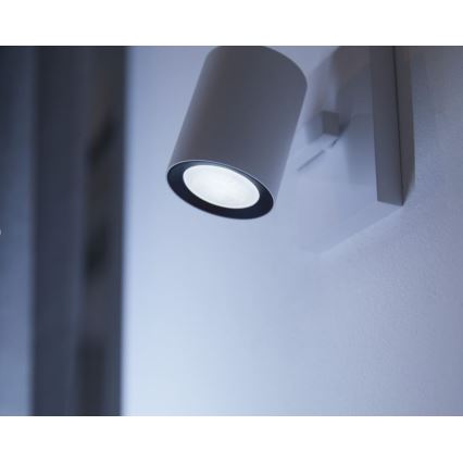 Biela nástenná lampa s valcovým telom svieti. Je pripevnená na svetlej stene.