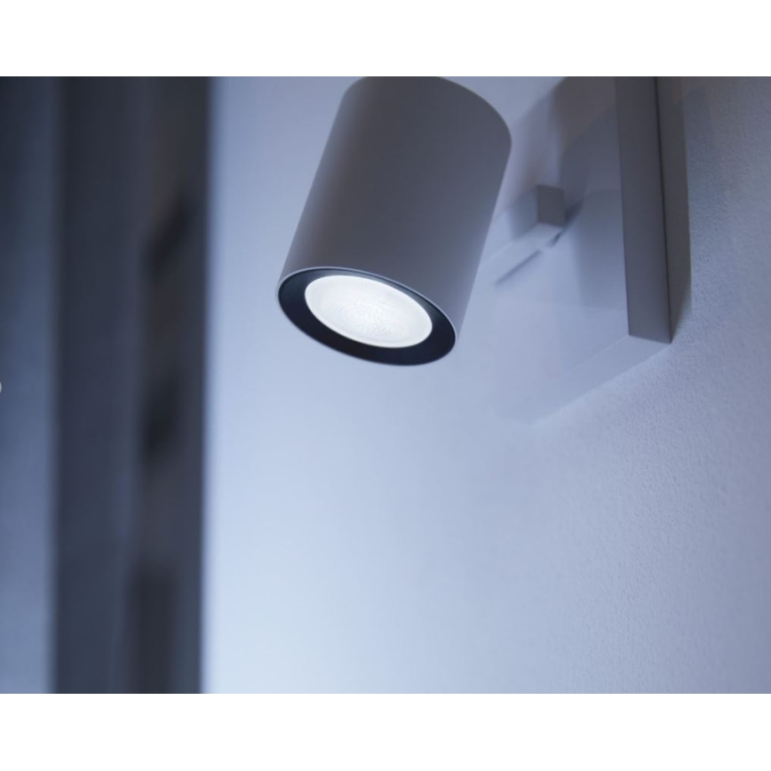 Biela nástenná lampa s valcovým telom svieti. Je pripevnená na svetlej stene.