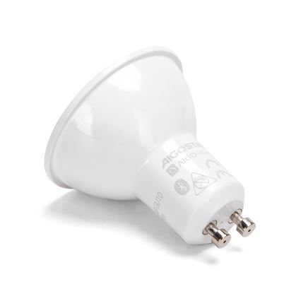 LED žiarovka GU10 leží na bielom pozadí. Na jej spodnej časti je viditeľné označenie: AIGOSTAR, AIGOSTAR SMART, symboly Bluetooth, zakázaného zdroja tepla a CE.