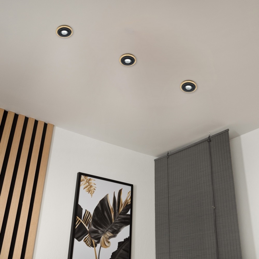 Tri vstavané stropné svetlá sú osadené na bielom strope. V miestnosti sa nachádza drevená stena, obraz s listami a tmavosivé žalúzie.