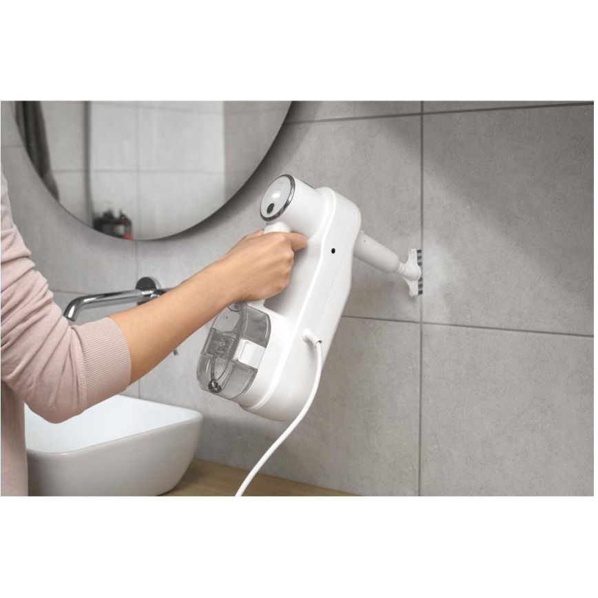 Žena používa biely parný čistič na čistenie dlaždíc v kúpeľni. Čistič je pripojený k elektrickej sieti a drží sa v ruke. Kúpeľňa obsahuje umývadlo a zrkadlo.