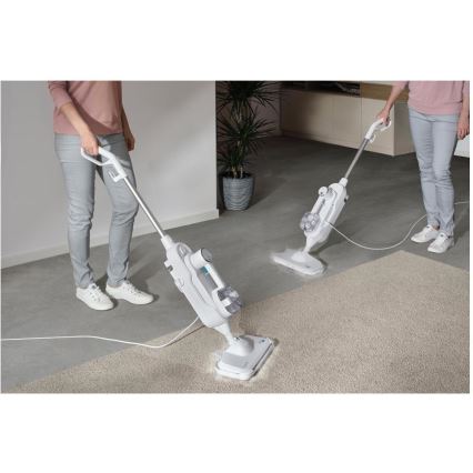 Dve osoby čistia parným čističom koberec v miestnosti. Čističe sú biele s modrými detailmi a sú pripojené k elektrickej sieti. V pozadí je vidieť rastlinu v kvetináči.